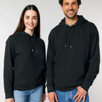 A woman and a man smiling and wearing plain black Stanley/Stella organic cotton hoodies with jeans.