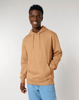 Young man smiling in a STSU177 Stella/Stella Cruiser 2.0 The Iconic Unisex Hoodie Sweatshirt and blue jeans against a neutral background.
