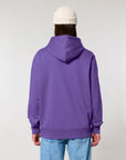 Person standing with their back to the camera wearing a purple STSU177 Stella/Stella Cruiser 2.0 The Iconic Unisex Hoodie Sweatshirt and a white beanie, paired with blue jeans.