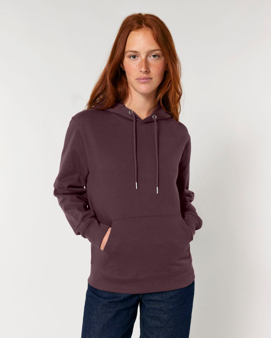 A woman with red hair wearing a maroon, STSU177 Stella/Stella Cruiser 2.0 The Iconic Unisex Hoodie Sweatshirt and jeans standing against a white background.