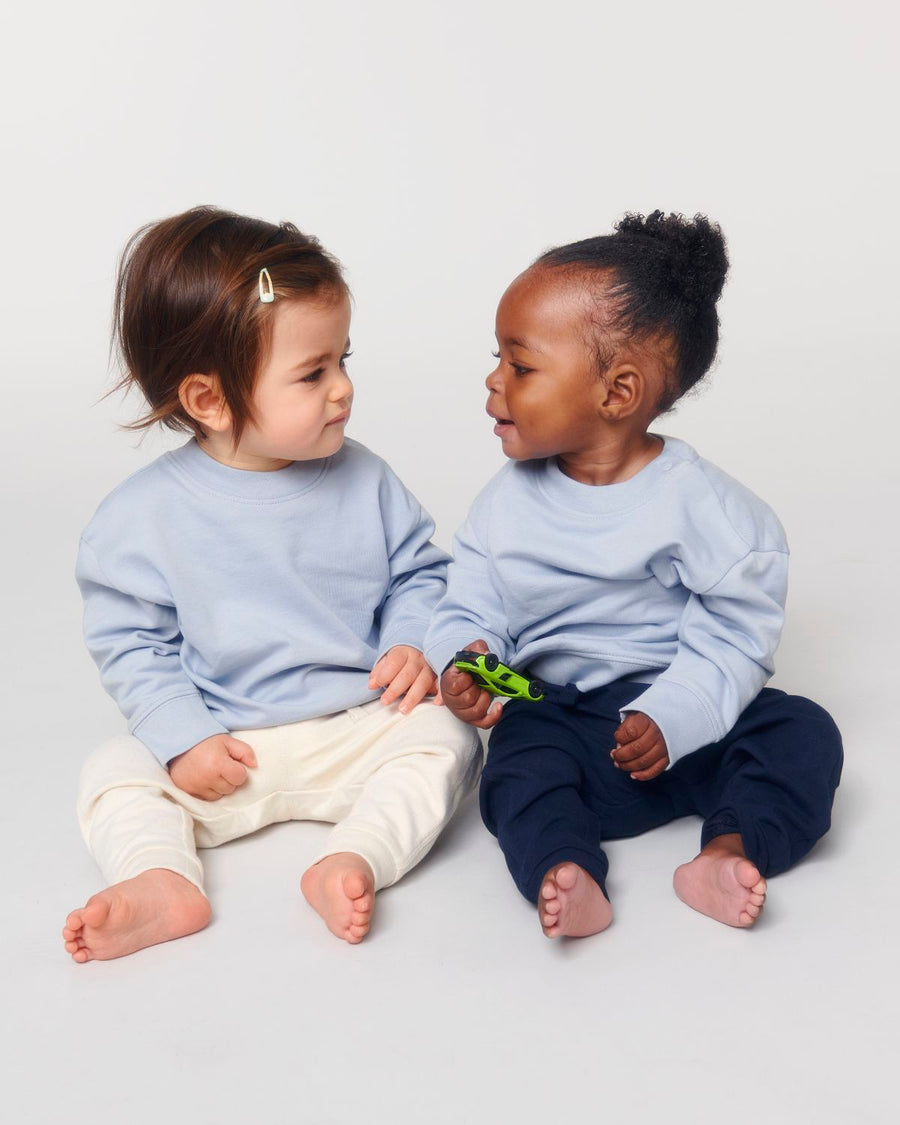 Two small children sitting on the floor in a blue Stanley/Stella babies' crew neck sweatshirt.