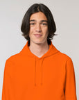 A man wearing a STSU812 Stanley/Stella Drummer Hoodie Bright Orange (C013) unisex sweatshirt.