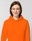 A woman wearing a STSU812 Stanley/Stella Drummer Hoodie Bright Orange (C013) unisex hoodie sweatshirt.