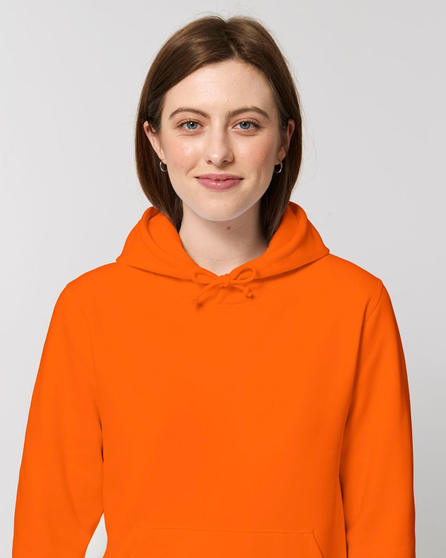 A woman wearing a STSU812 Stanley/Stella Drummer Hoodie Bright Orange (C013) unisex hoodie sweatshirt.