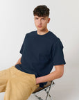 A man sitting on a chair wearing a navy STTU788 Stanley/Stella Freestyler Heavy Organic Cotton Unisex T-shirt and khaki pants made of organic cotton.