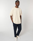 A man wearing a cream STTU788 Stanley/Stella Freestyler Heavy Organic Cotton Unisex T-shirt and navy pants made from organic cotton.