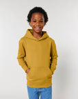 A young boy wearing a STSK180 Stella/Stella Mini Cruiser 2.0 The Iconic Kids Hoodie Sweatshirt in yellow and jeans.