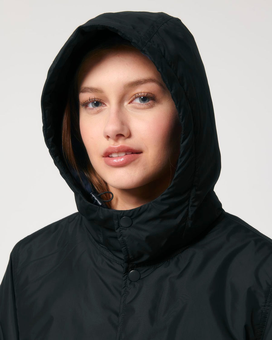 A woman wearing a black hooded STJU841 Stanley/Stella Padded Parker Jacket.