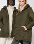A man and a woman wearing a STJU841 Stanley/Stella Padded Parker Jacket decorated in green.
