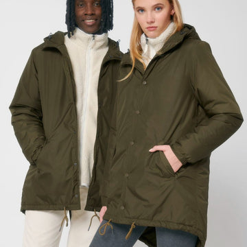A man and a woman wearing a STJU841 Stanley/Stella Padded Parker Jacket decorated in green.