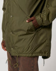 A man wearing a STJU841 Stanley/Stella padded green parka jacket with a hood.