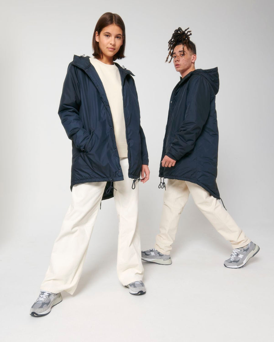 A woman and a man in a navy STJU841 Stanley/Stella Padded Parka and white pants.