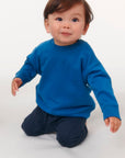 A baby in a blue organic ring-spun cotton STSB920 Stella/Stella Baby Changer The Iconic Babies' Crew Neck Sweatshirt.