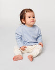 A baby sitting on the floor in a STSB920 Stella/Stella Baby Changer The Iconic Babies' Crew Neck Sweatshirt.