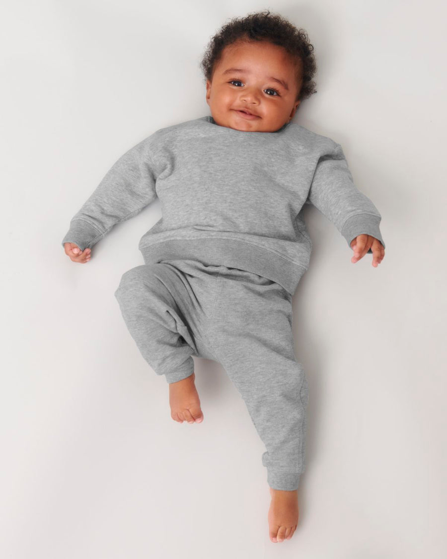 A baby laying on a white surface in a STSB920 Stella/Stella Baby Changer The Iconic Babies' Crew Neck Sweatshirt.