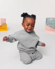A baby sitting on the floor in a grey sweatsuit made from organic ring-spun cotton STSB920 Stanley/Stella Baby Changer The Iconic Babies' Crew Neck Sweatshirt.
