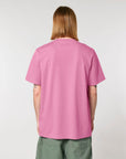 Person with long hair facing away, wearing a pink, STTU171 Stanley/Stella Sparker 2.0 The Unisex Heavy T-Shirt made of organic carded cotton and green shorts against a plain background.