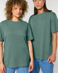 Two individuals, one with curly hair and the other with straight hair, are standing side by side wearing matching Stanley/Stella STTU171 Stanley/Stella Sparker 2.0 The Unisex Heavy T-Shirts made from organic carded cotton and blue jeans. Both are looking directly at the camera.