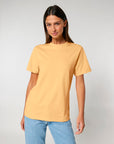 A woman with long brown hair is wearing a plain yellow STTU171 Stanley/Stella Sparker 2.0 The Unisex Heavy T-Shirt made from organic carded cotton and light blue jeans, standing against a plain light gray background.