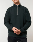 A man wearing a STSM611 Stanley Trucker Men's Quarter Zip Organic Cotton Sweatshirt made of recycled polyester and jeans.