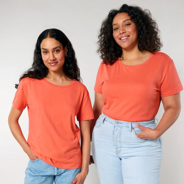 Two women smiling and posing in casual orange Stanley/Stella STTW173 Stella Serena Mid-Light scoop neck t-shirts and blue jeans against a neutral background.