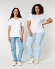 Two individuals stand side by side against a plain background, both wearing white STTW173 Stella Serena Mid-Light Scoop Neck T-Shirts from Stanley/Stella made from 100% organic cotton, paired with light blue jeans and white sneakers.